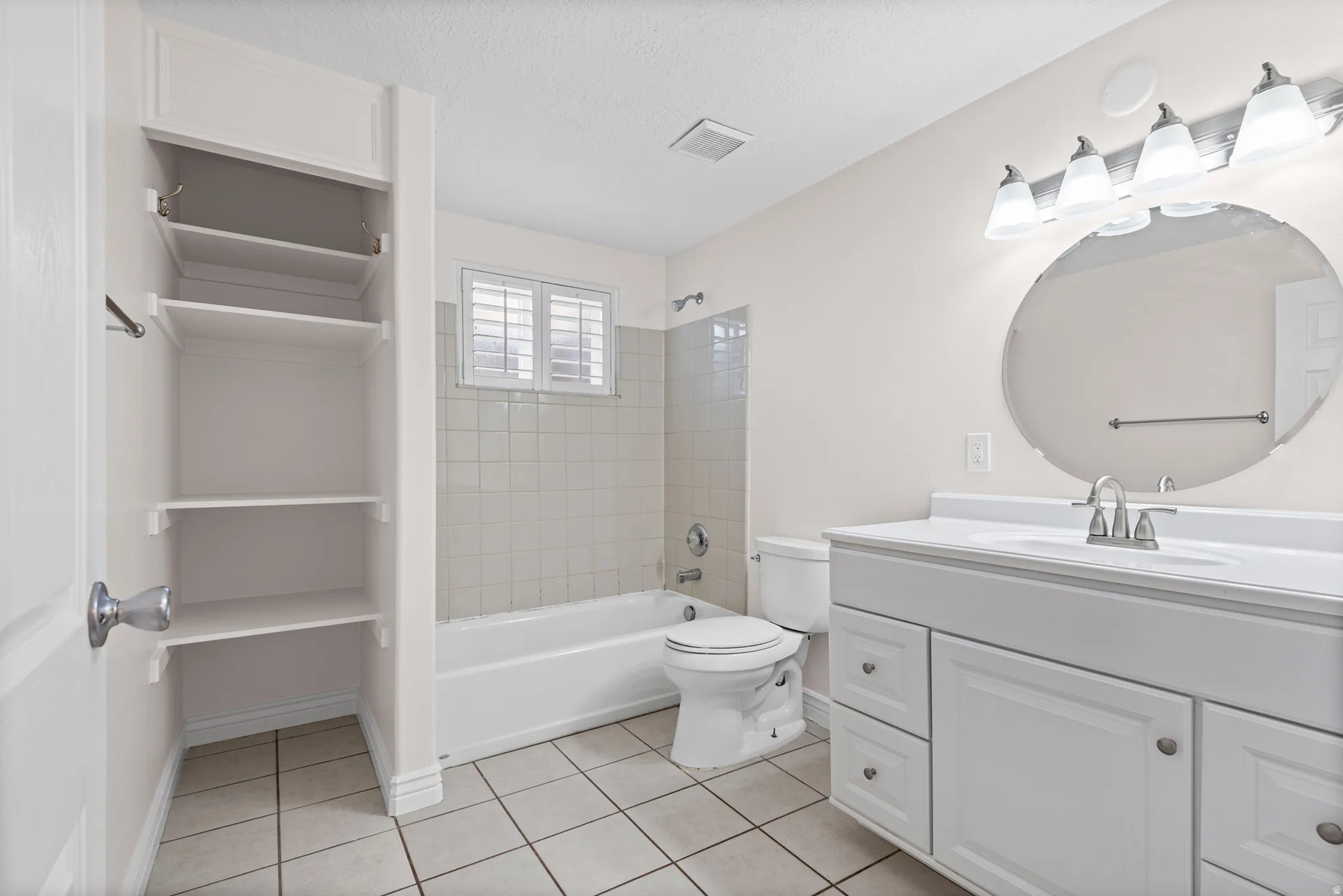 Full bathroom featuring a white vanity with integrated sink, a rectangular mirror, a bathtub with tile surround, and built-in shelving
