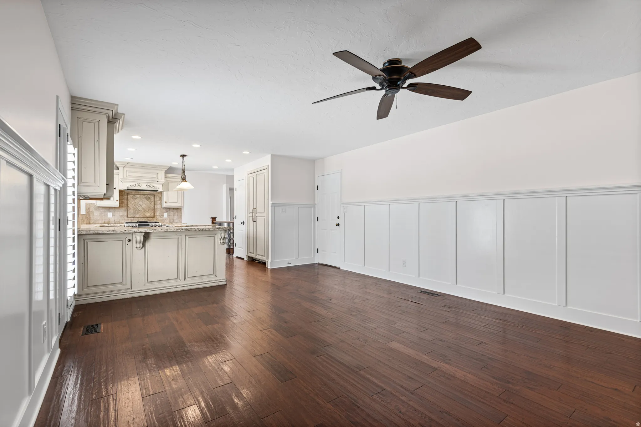 Open-concept living space with dark wood-finish flooring, white wainscoting, and a ceiling fan