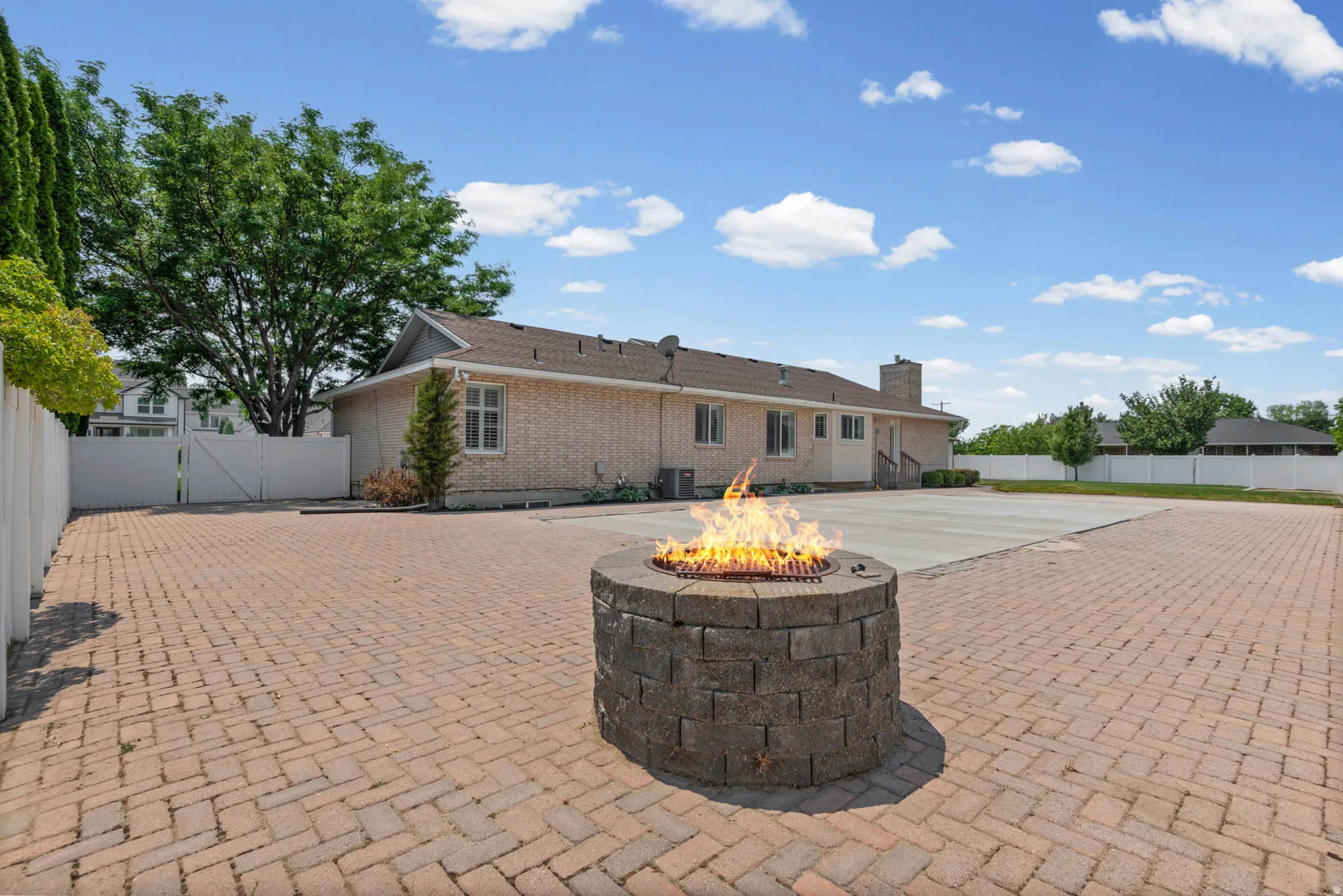 Spacious outdoor patio featuring a stone fire pit, extensive brick paver flooring, and a large concrete area