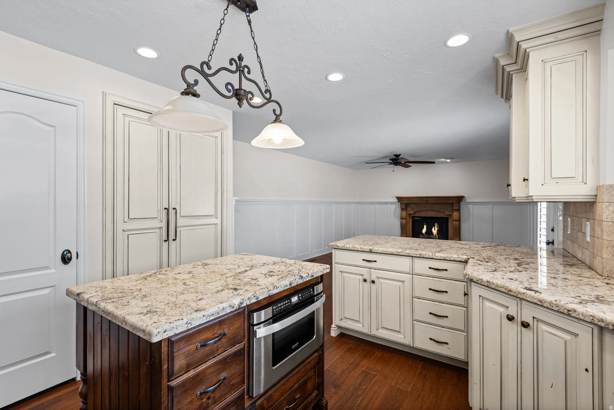 Kitchen featuring two islands with stone countertops, a built-in microwave, white cabinetry, and wood-finish flooring