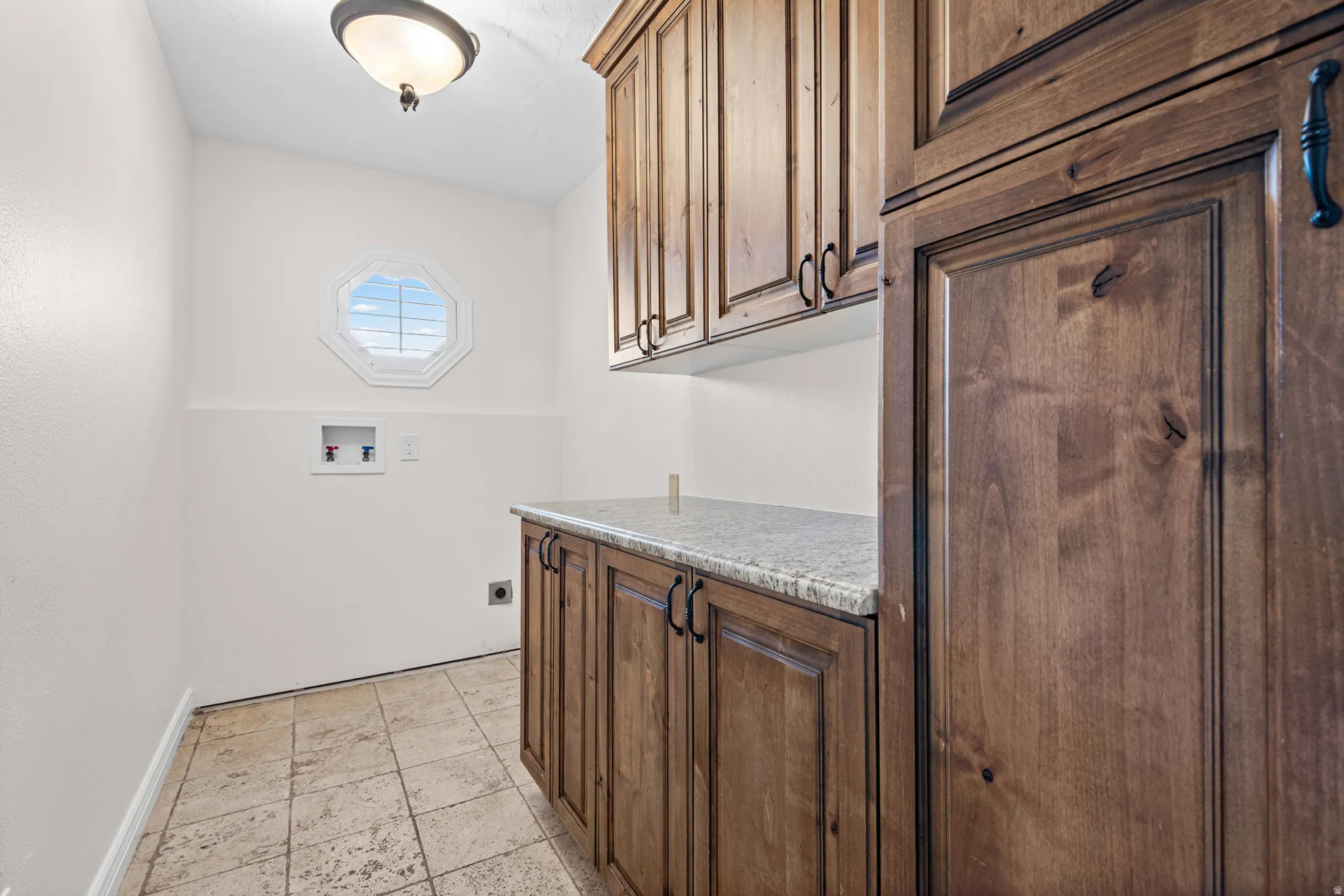 Laundry area featuring wood-finish cabinetry, light-toned stone countertop, and tile flooring
