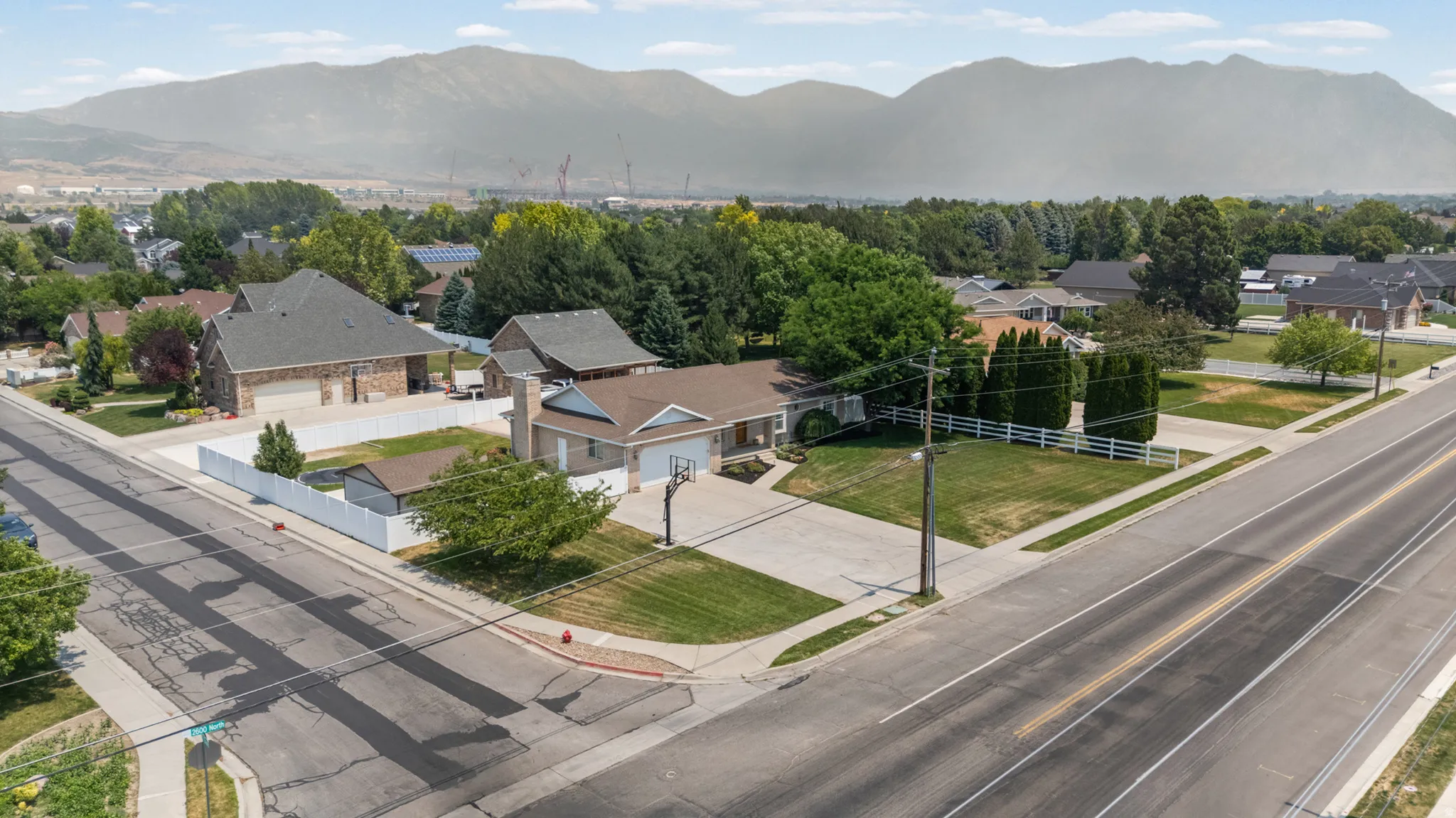 Single-story residence on a corner lot featuring a white vinyl fence, mature landscaping, and a paved driveway