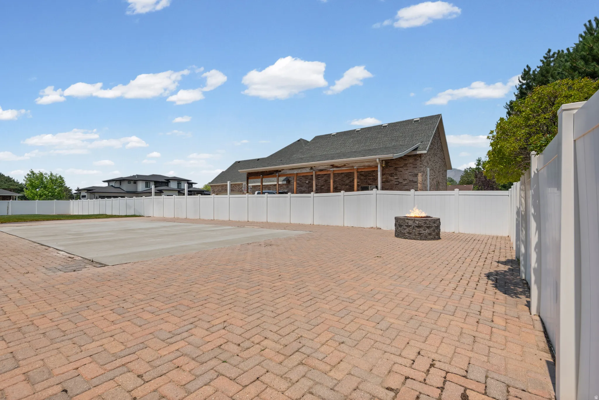 Expansive herringbone-patterned brick paver patio featuring a built-in stone fire pit