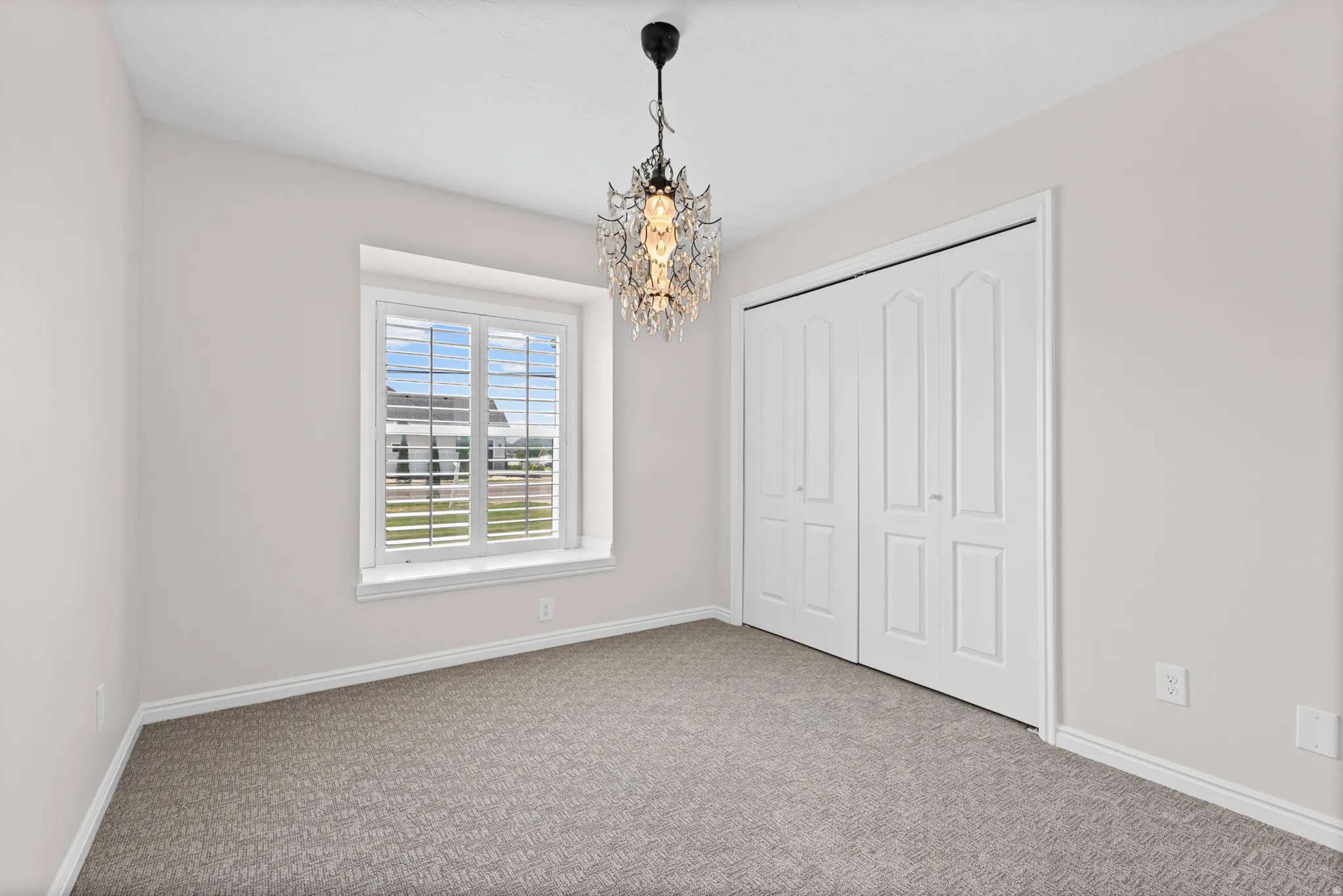 Bedroom featuring a decorative chandelier, window with plantation shutters, neutral carpeting, and bi-fold closet doors