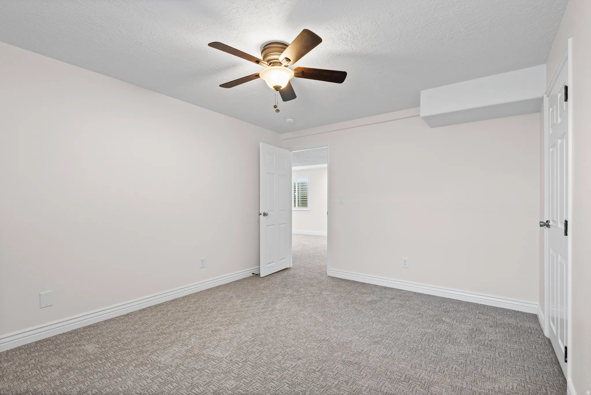 Carpeted room with a ceiling fan light fixture, white interior door, and a wall-mounted air conditioning unit
