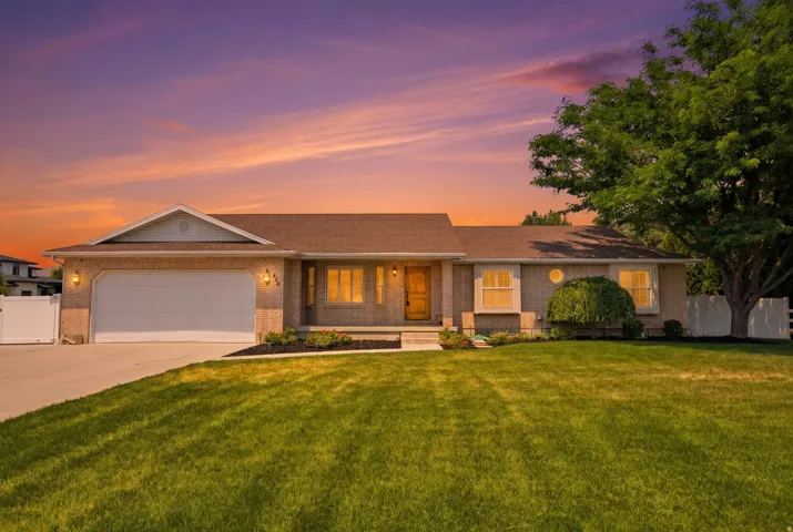 Brick exterior featuring a two-car garage, mature landscaping, front entry porch, and a fenced yard