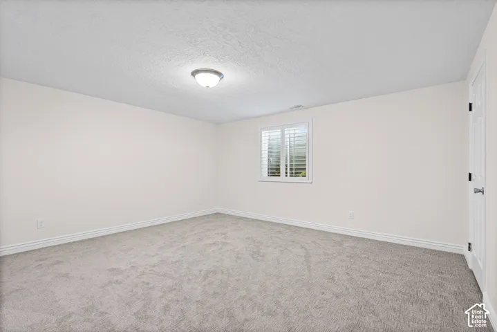 Spacious room featuring neutral carpet flooring, light-toned walls, and a window with white louvered blinds