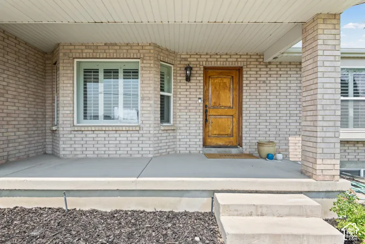 Brick facade featuring a natural wood-finish entry door, an exterior sconce, and a bay window with louvered blinds