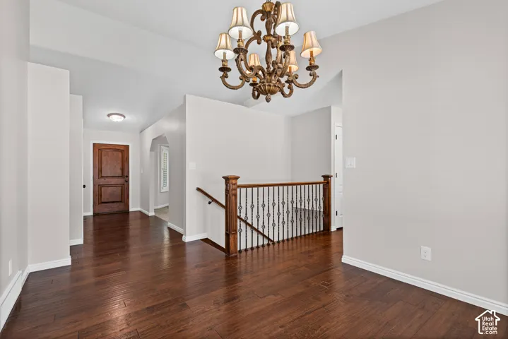 Elegant foyer featuring wood-finish flooring, a decorative chandelier, a detailed wooden entry door, and a staircase with wrought iron balusters and a wood handrail