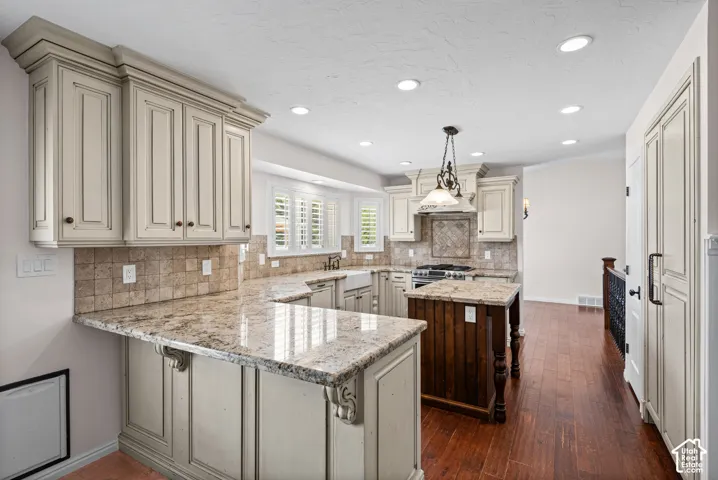 Kitchen featuring U-shaped stone countertops, custom cabinetry with crown molding, a tiled backsplash, and recessed lighting