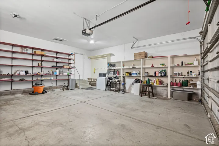 Spacious garage featuring a concrete floor, built-in shelving, overhead lighting, and an automatic garage door opener