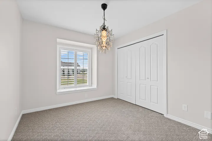 Bedroom featuring a decorative chandelier, window with plantation shutters, neutral carpeting, and bi-fold closet doors