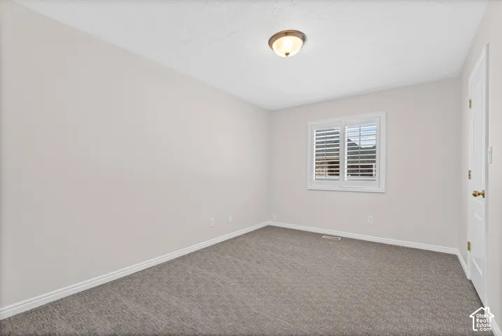 Neutral-toned room featuring a window with white plantation shutters, textured carpeting, and a flush-mount ceiling light fixture