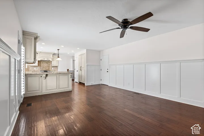 Open-concept living space with dark wood-finish flooring, white wainscoting, and a ceiling fan