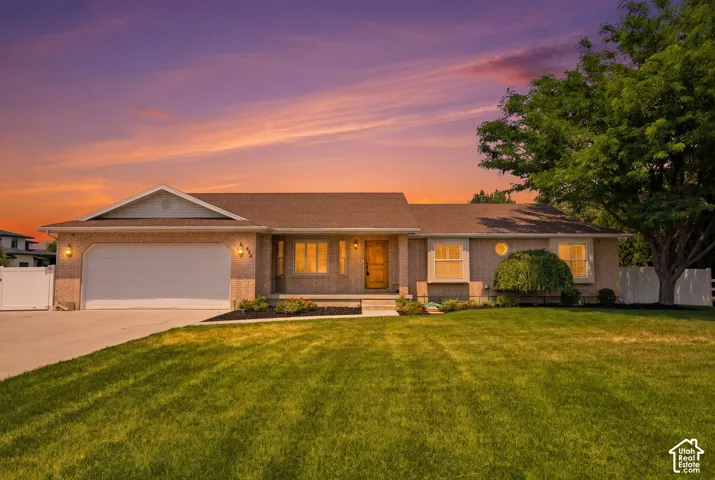 Brick exterior featuring a two-car garage, mature landscaping, front entry porch, and a fenced yard
