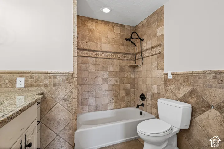 Bathroom featuring a built-in bathtub with a dark-finish shower fixture, tile surround, and a coordinating tiled toilet area