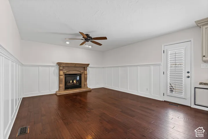 Living space featuring a stone-clad fireplace with a dark insert, dark wood-finish flooring, white wainscoting, and a ceiling fan with integrated lighting