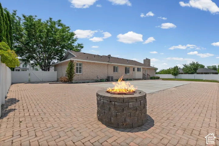Spacious outdoor patio featuring a stone fire pit, extensive brick paver flooring, and a large concrete area
