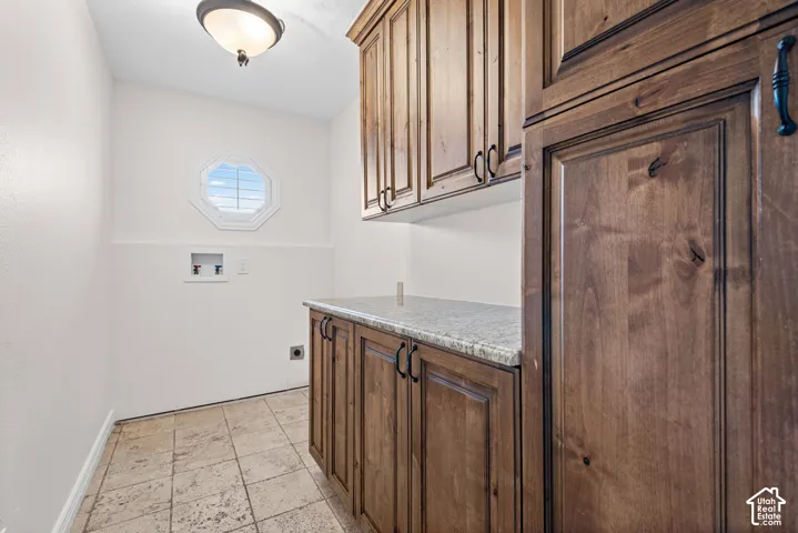 Laundry area featuring wood-finish cabinetry, light-toned stone countertop, and tile flooring