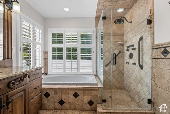 Tiled bathroom featuring a glass-enclosed shower, built-in bathtub, and a wood-finish vanity with a stone countertop