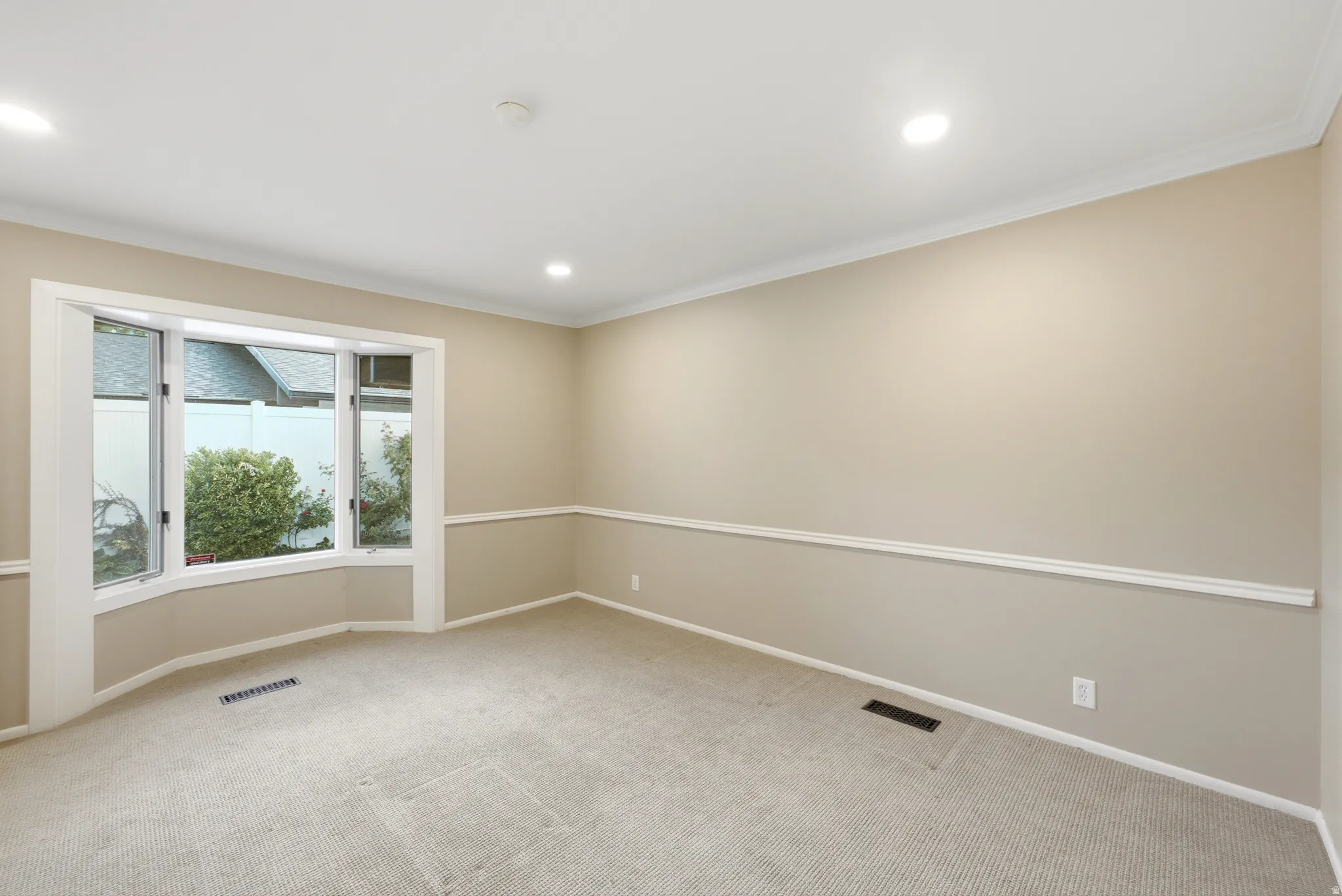 Carpeted room featuring a bay window, crown molding, chair rail molding, recessed lighting, and neutral wall tones