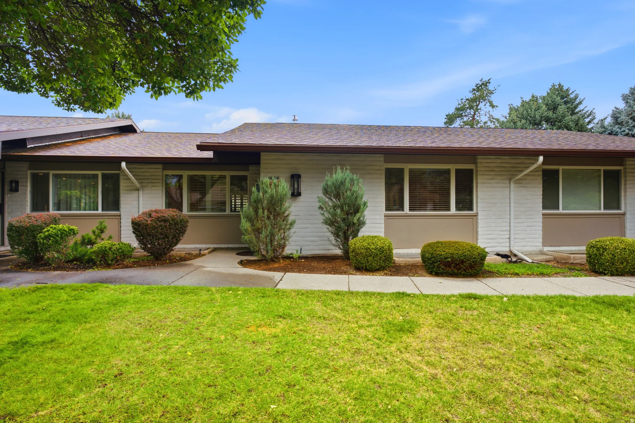 Single-story residence featuring white brick and tan paneling, a brown shingle roof, and a green lawn