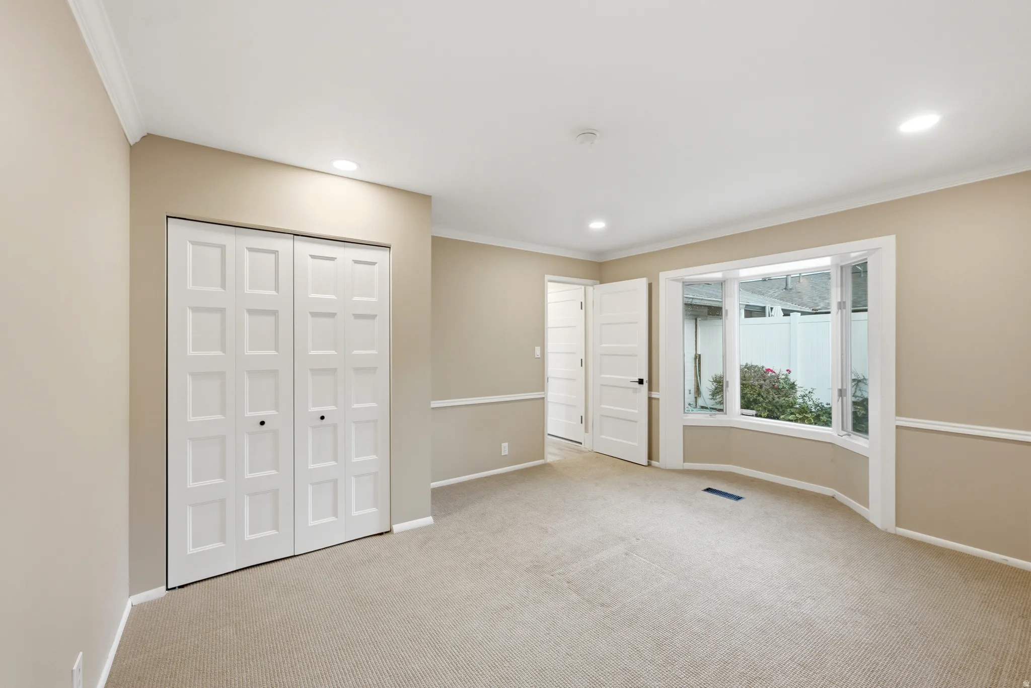 Carpeted room with a bay window, recessed lighting, crown molding, and wainscoting