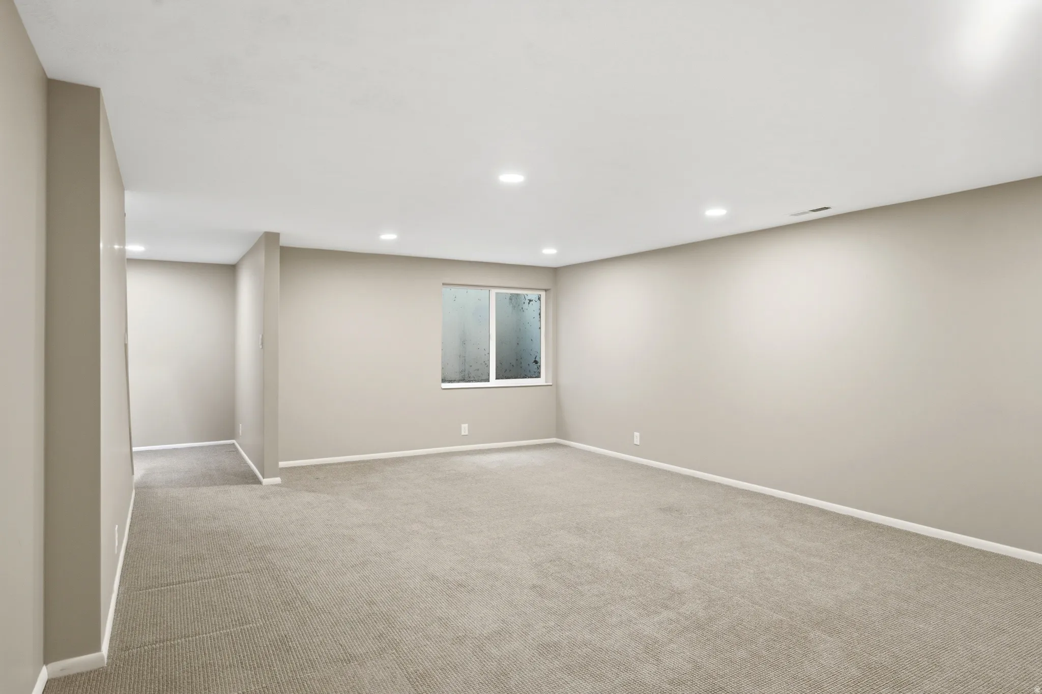 Spacious room featuring neutral carpeting, recessed ceiling lighting, a single window, and light-toned wall finishes