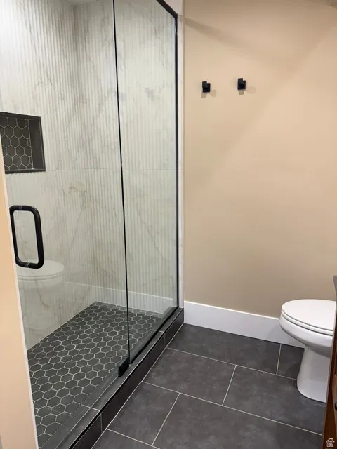 Enclosed shower featuring a clear glass door with black trim and hardware, a gray hexagonal tile shower pan, and a recessed shower niche