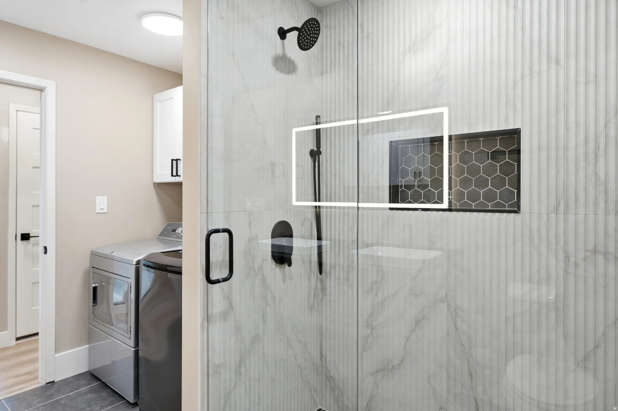 Glass-enclosed shower with matte black fixtures, integrated storage niche with hexagonal tile, and vertical fluted wall tile