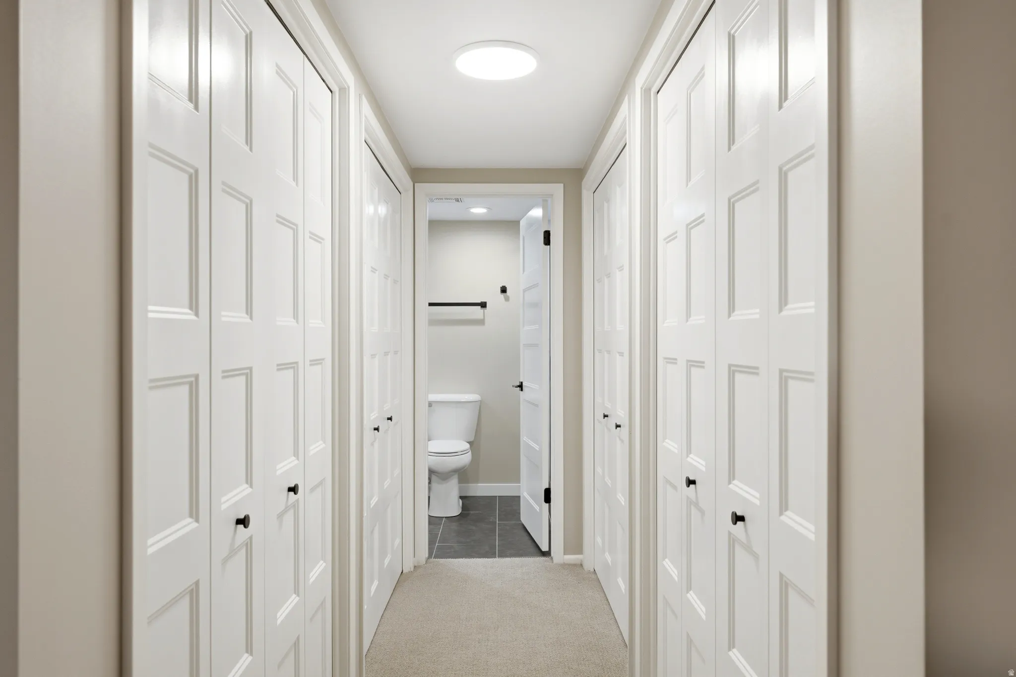 Hallway featuring numerous paneled bifold closet doors, a circular ceiling light fixture, and neutral wall paint