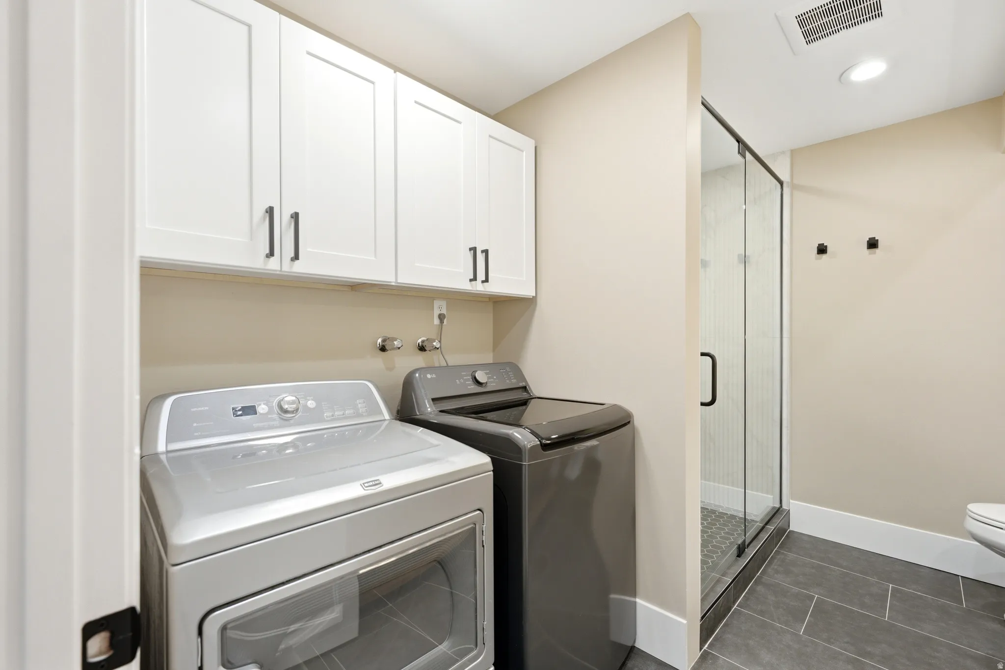 Laundry area featuring white shaker-style cabinetry with dark hardware and a full-size front-loading washing machine and dryer