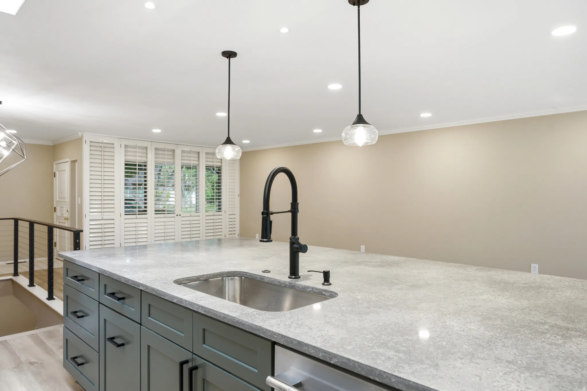 Kitchen island featuring an undermount stainless steel sink with a matte black high-arc faucet, light-toned countertop, and dark cabinetry with matte black hardware
