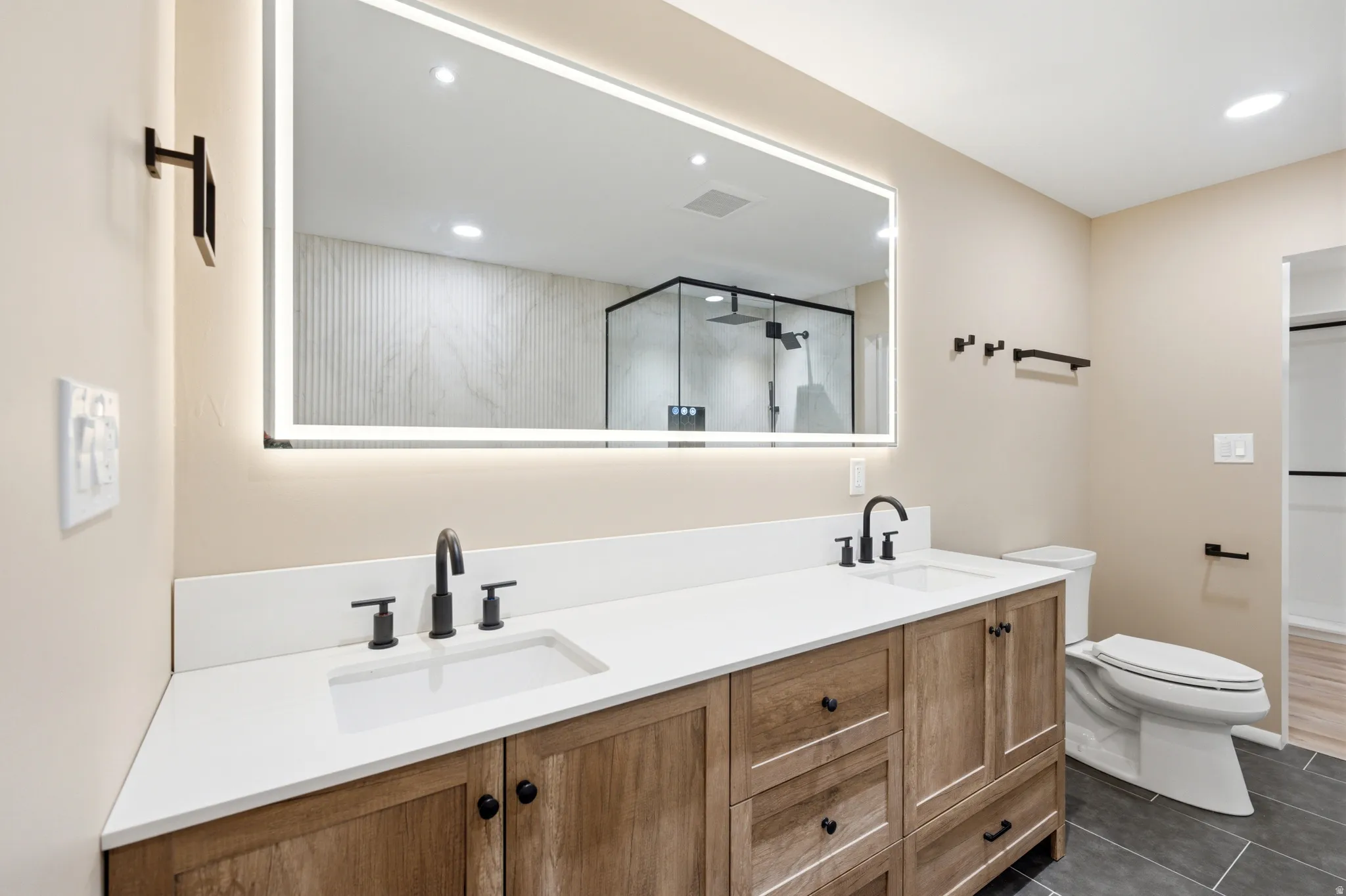 Double vanity with wood-finish cabinetry, white countertops, and matte black fixtures