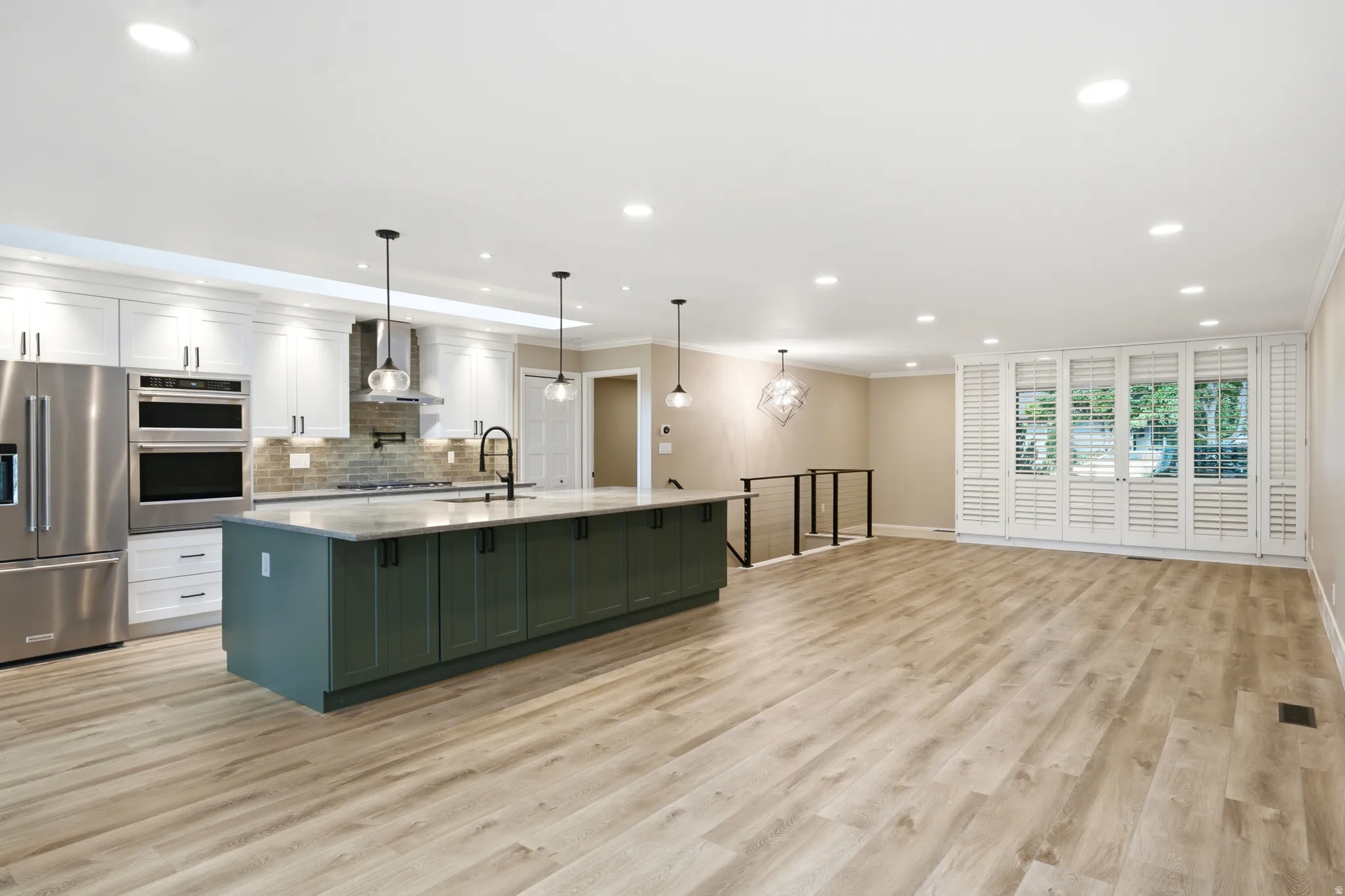Spacious open-concept kitchen and living area featuring wood-finish flooring, recessed lighting, and a multi-panel window with louvered shutters