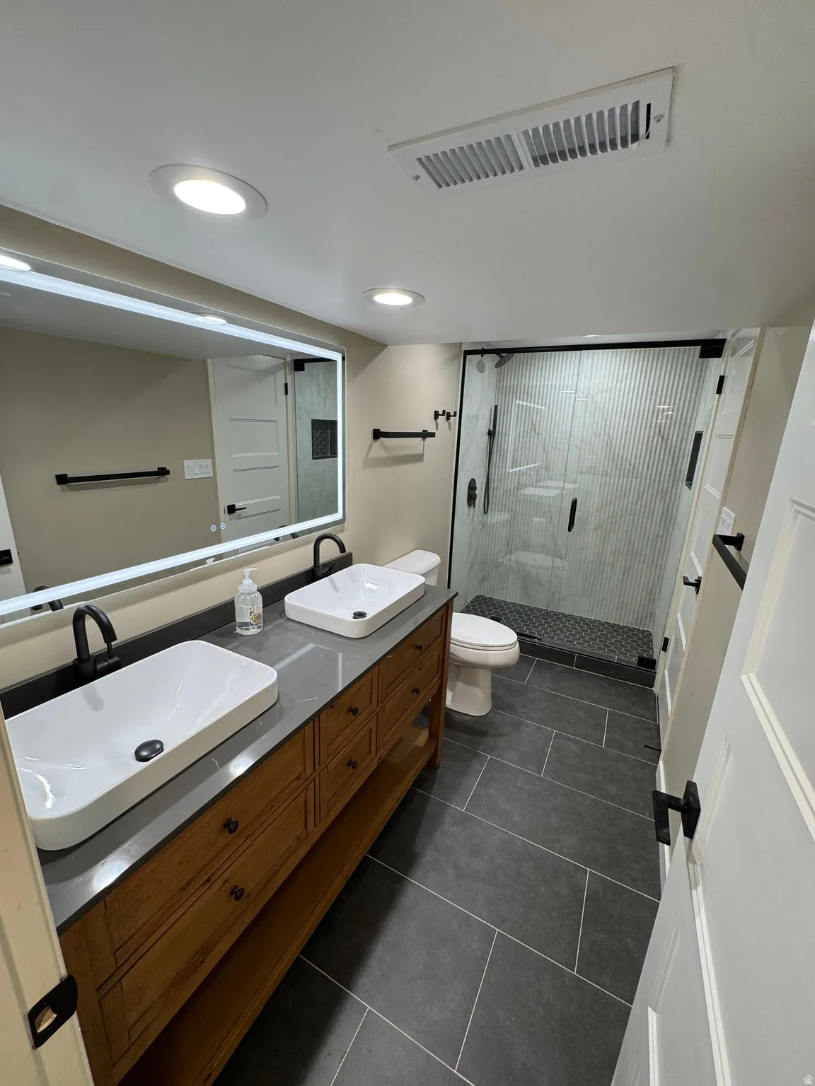 Bathroom with dual vessel sinks, wood-finish vanity, and a gray countertop