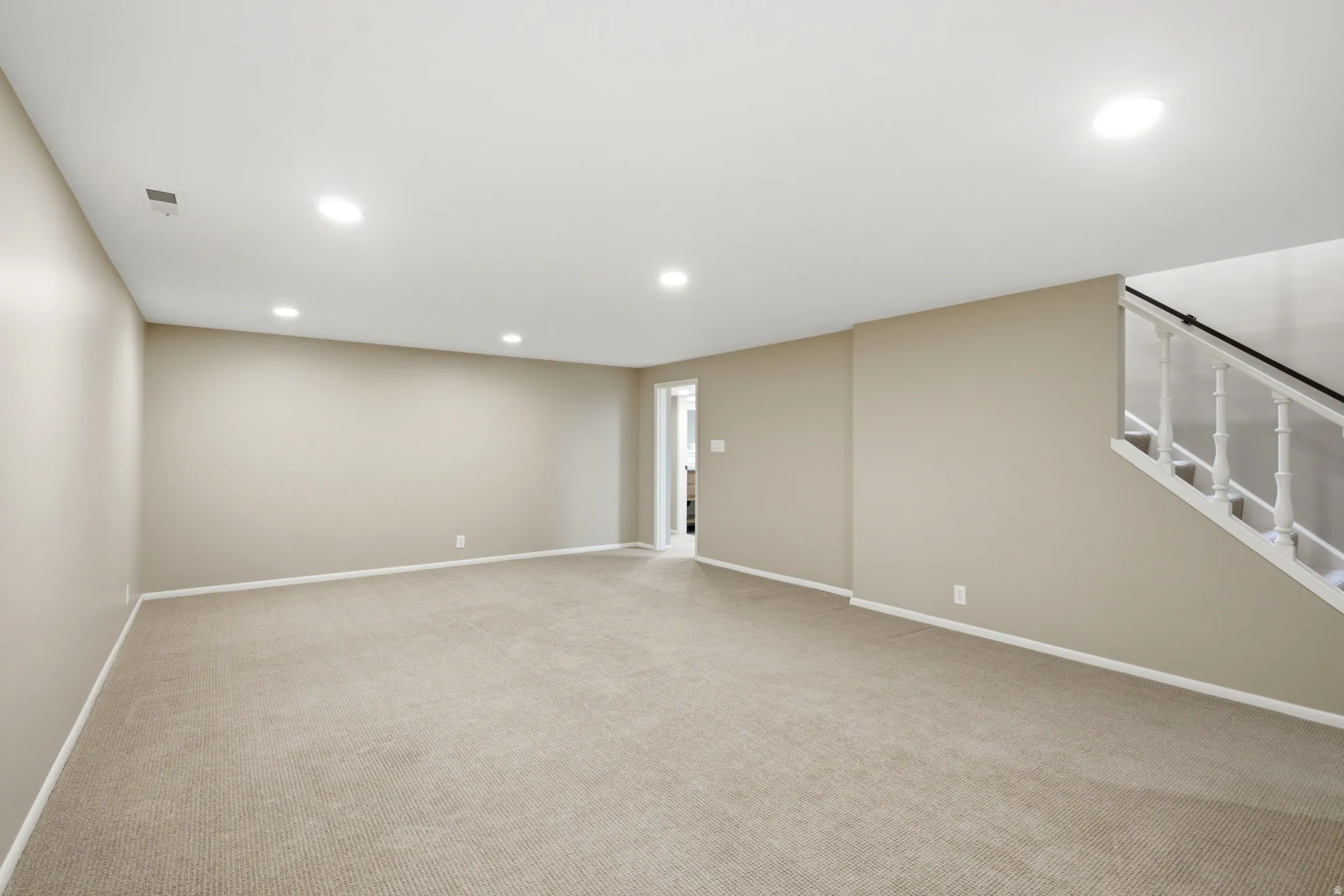 Spacious carpeted room featuring neutral wall paint, recessed lighting, and white baseboards