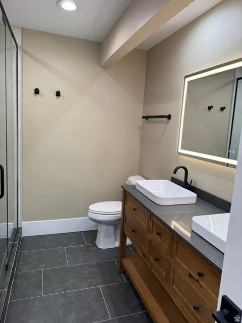 Bathroom featuring a double vanity with wood-finish cabinetry and vessel sinks, dark countertop, and an illuminated mirror