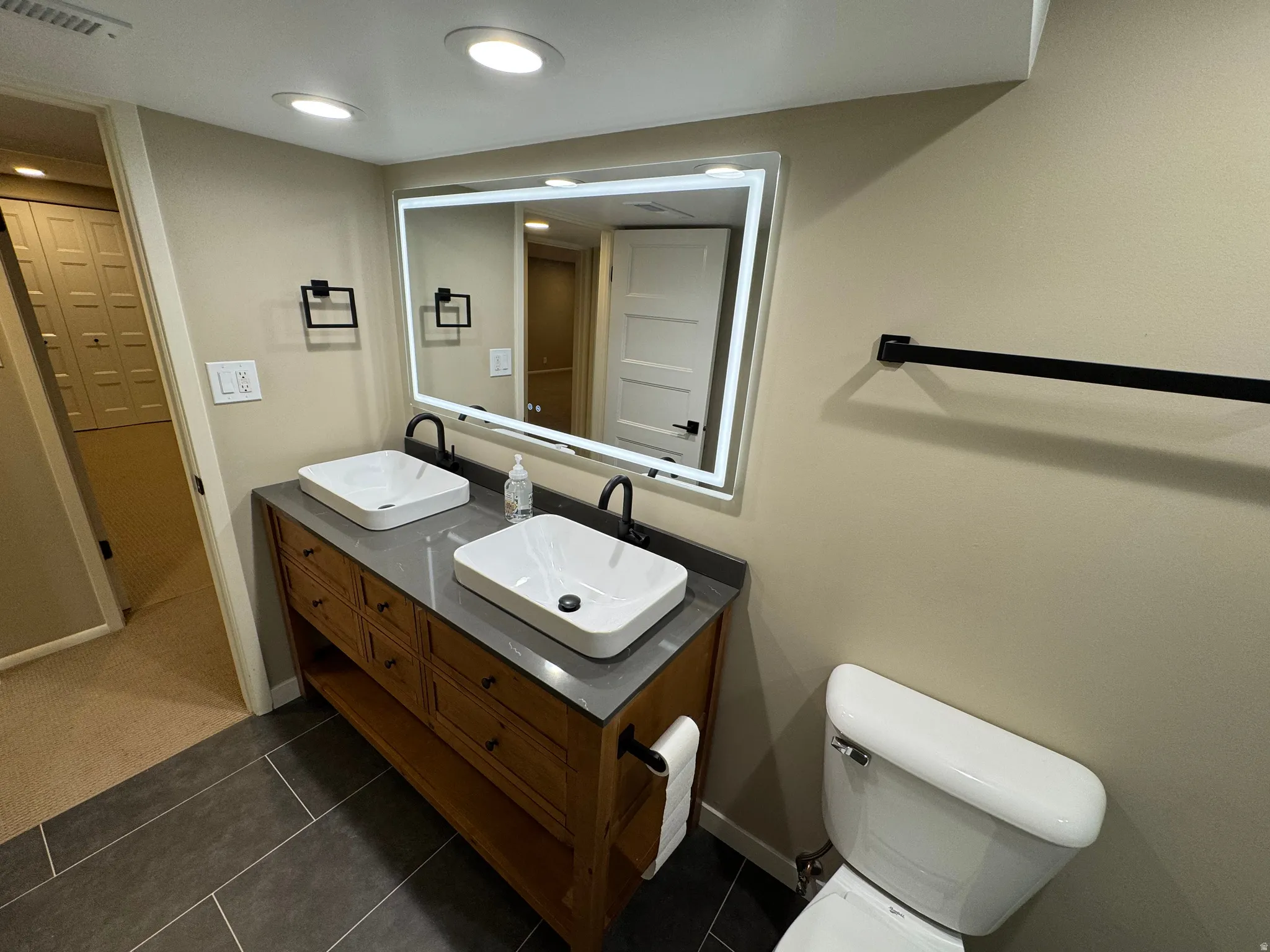 Modern bathroom featuring a dual vessel sink vanity with a grey countertop, dark wood-finish cabinetry, and matte black fixtures