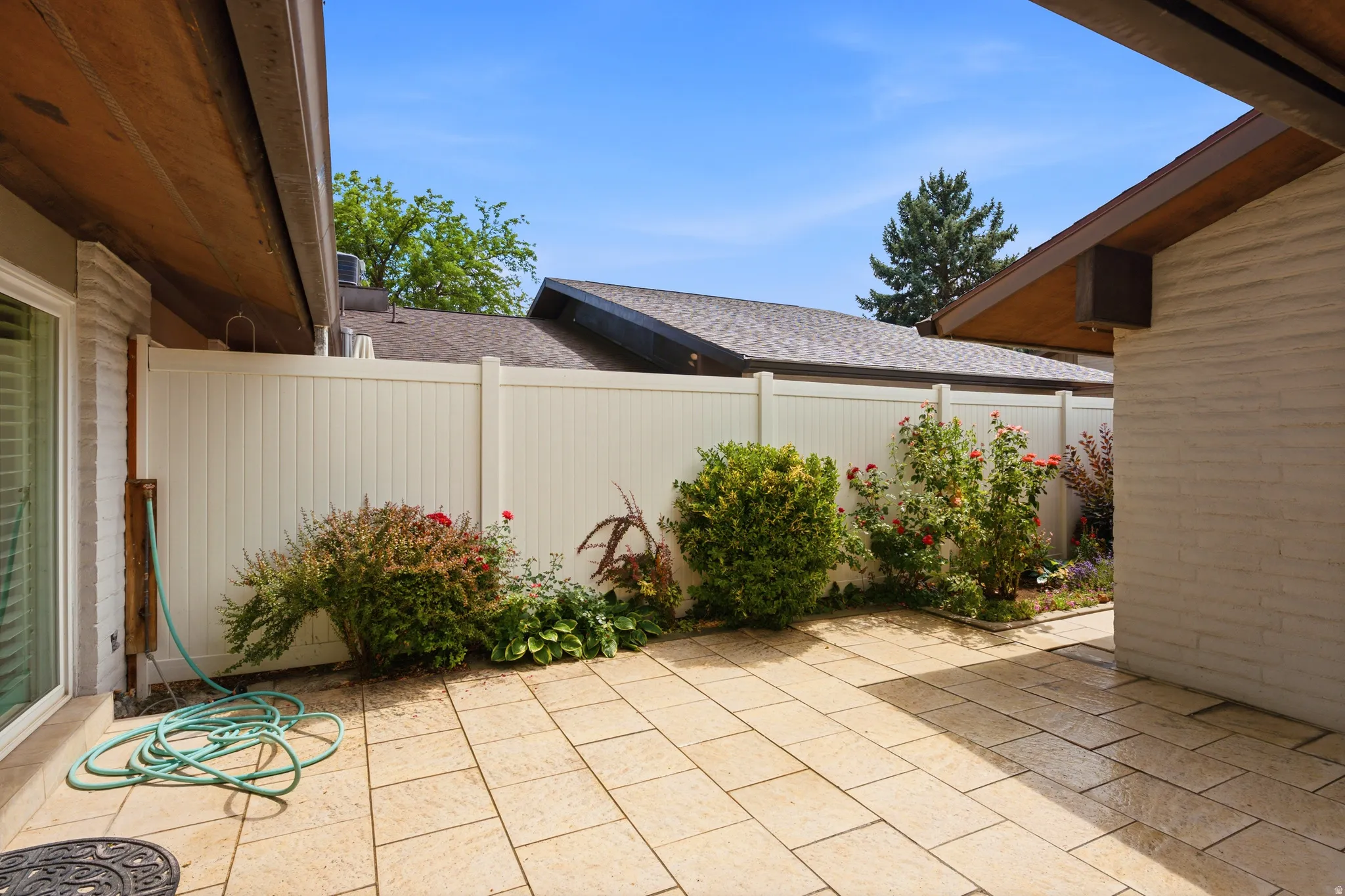 Outdoor patio featuring light-toned pavers, a white privacy fence, and diverse plantings