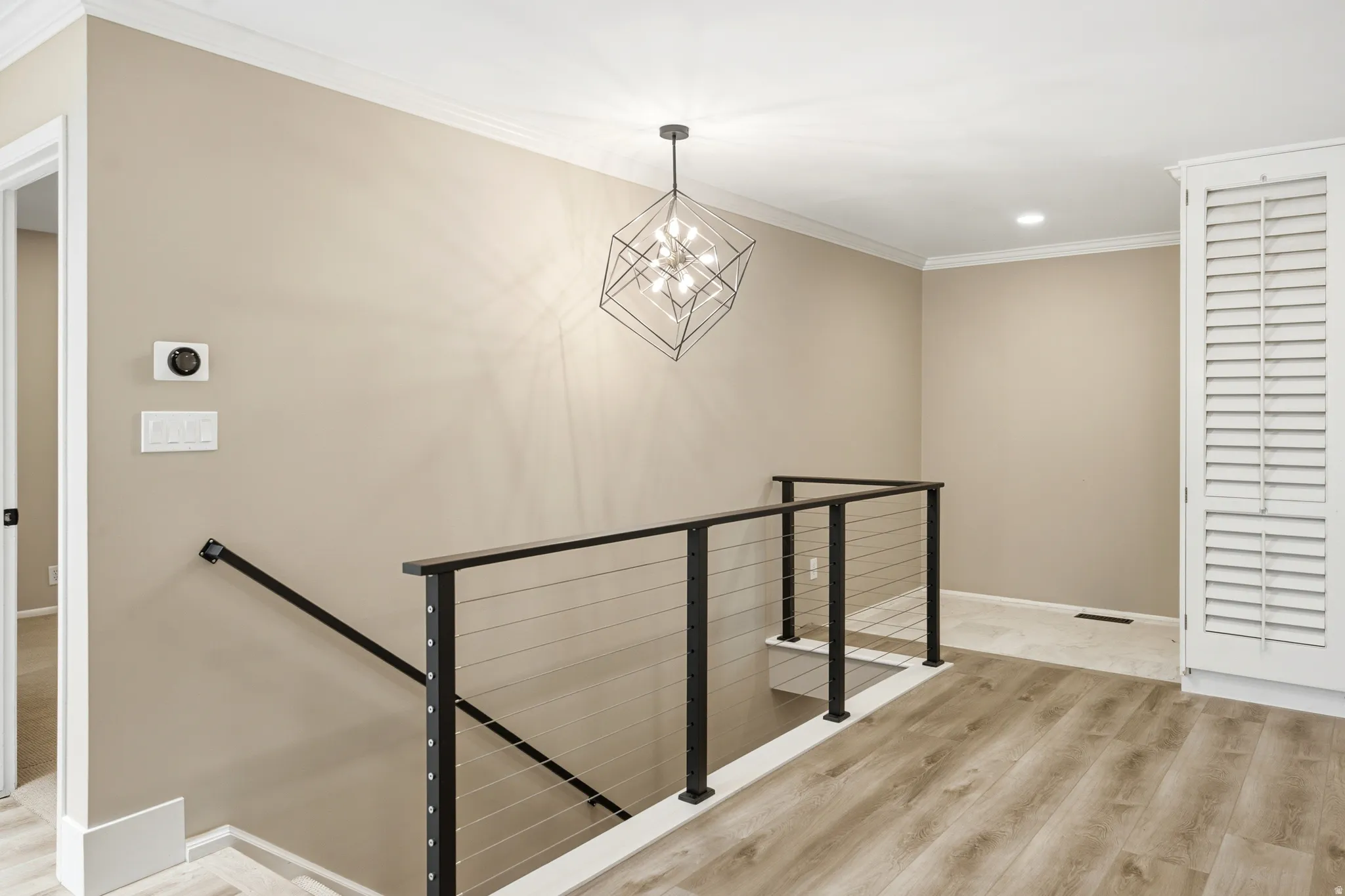 Modern stairwell featuring a black metal railing with cable infill, wood-finish flooring, and a contemporary geometric chandelier