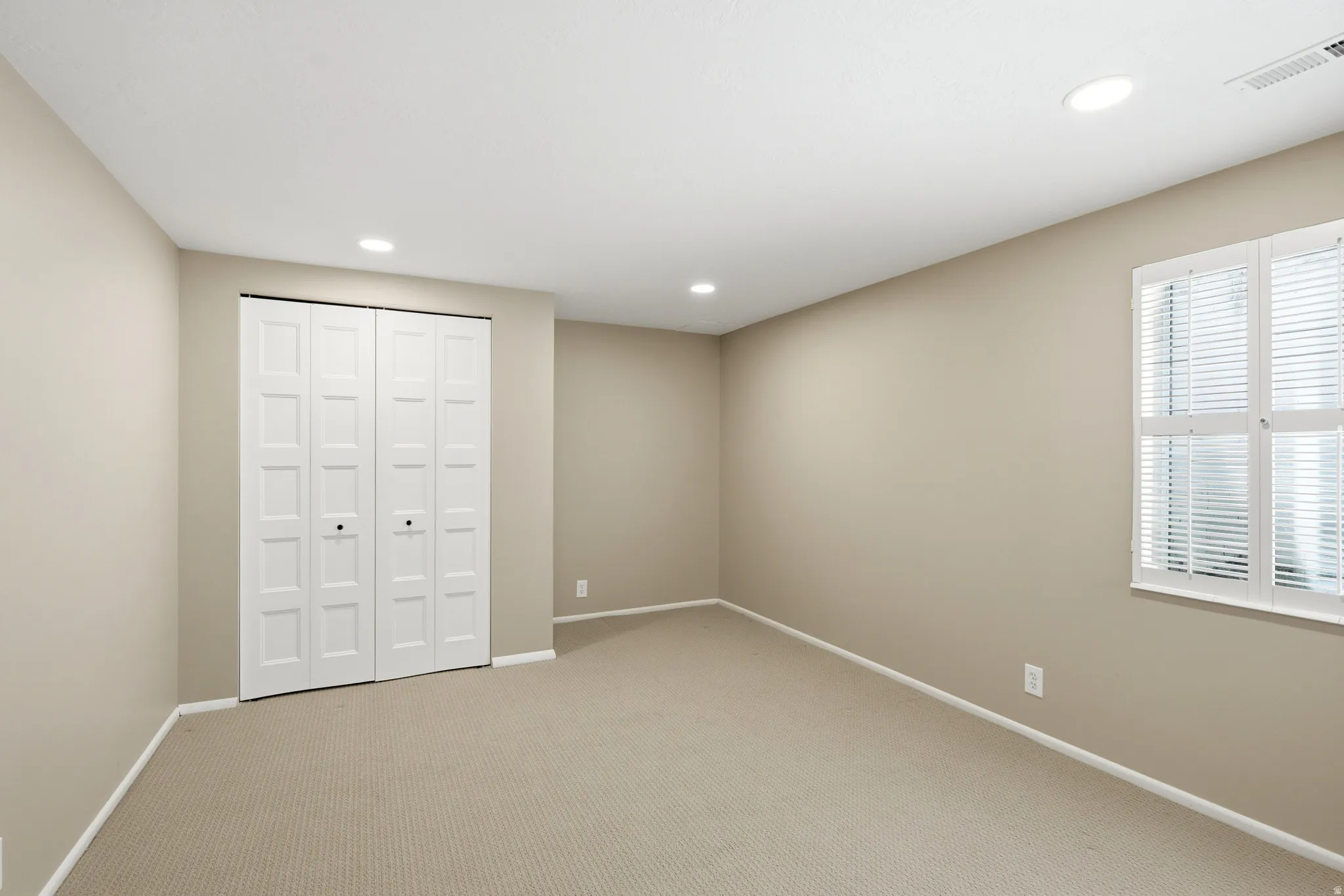 Neutral-toned room featuring a window with white shutters, dual bi-fold closet doors, recessed lighting, and carpet flooring
