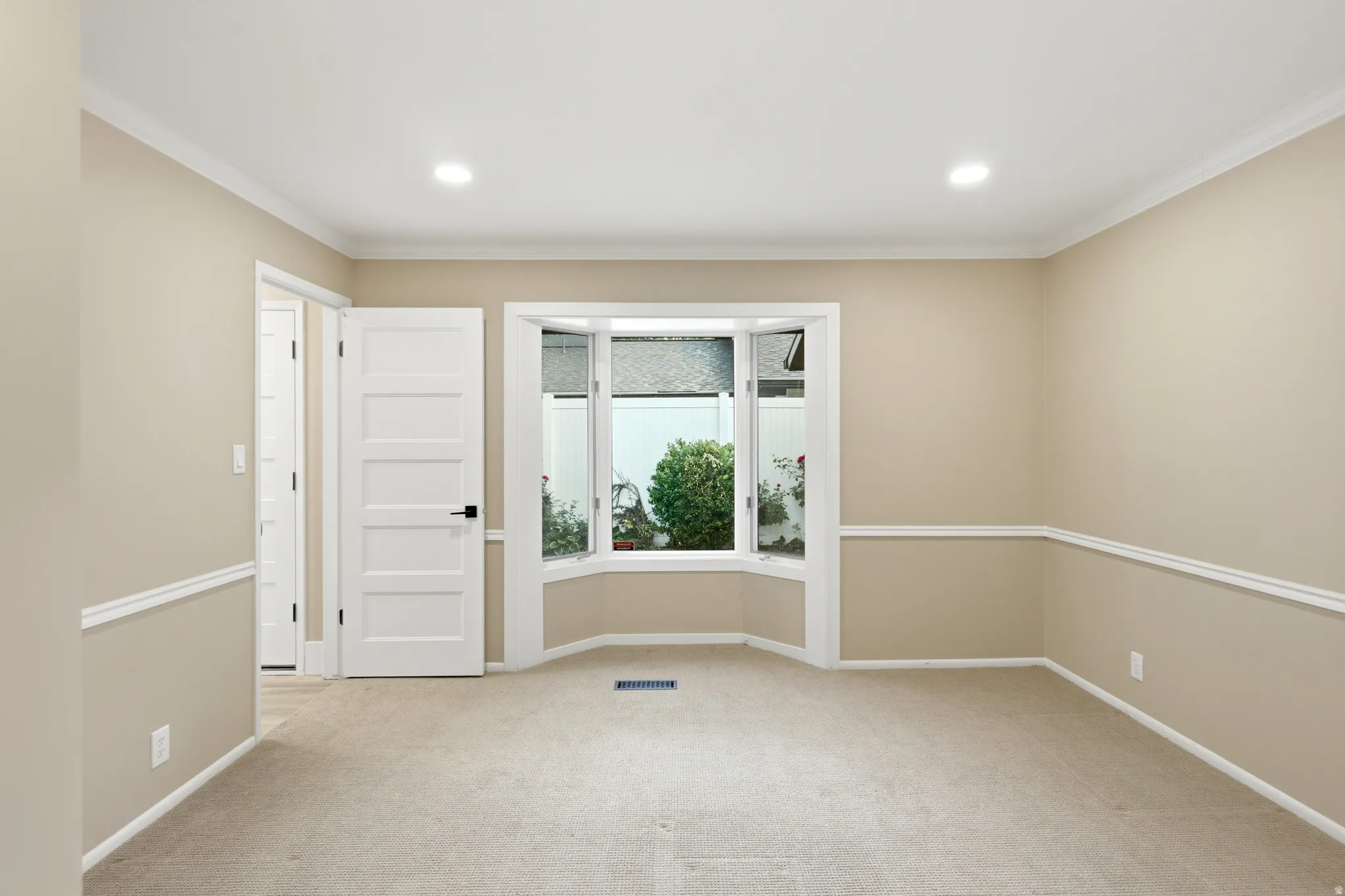 Carpeted room featuring a bay window, recessed lighting, crown molding, and wainscoting