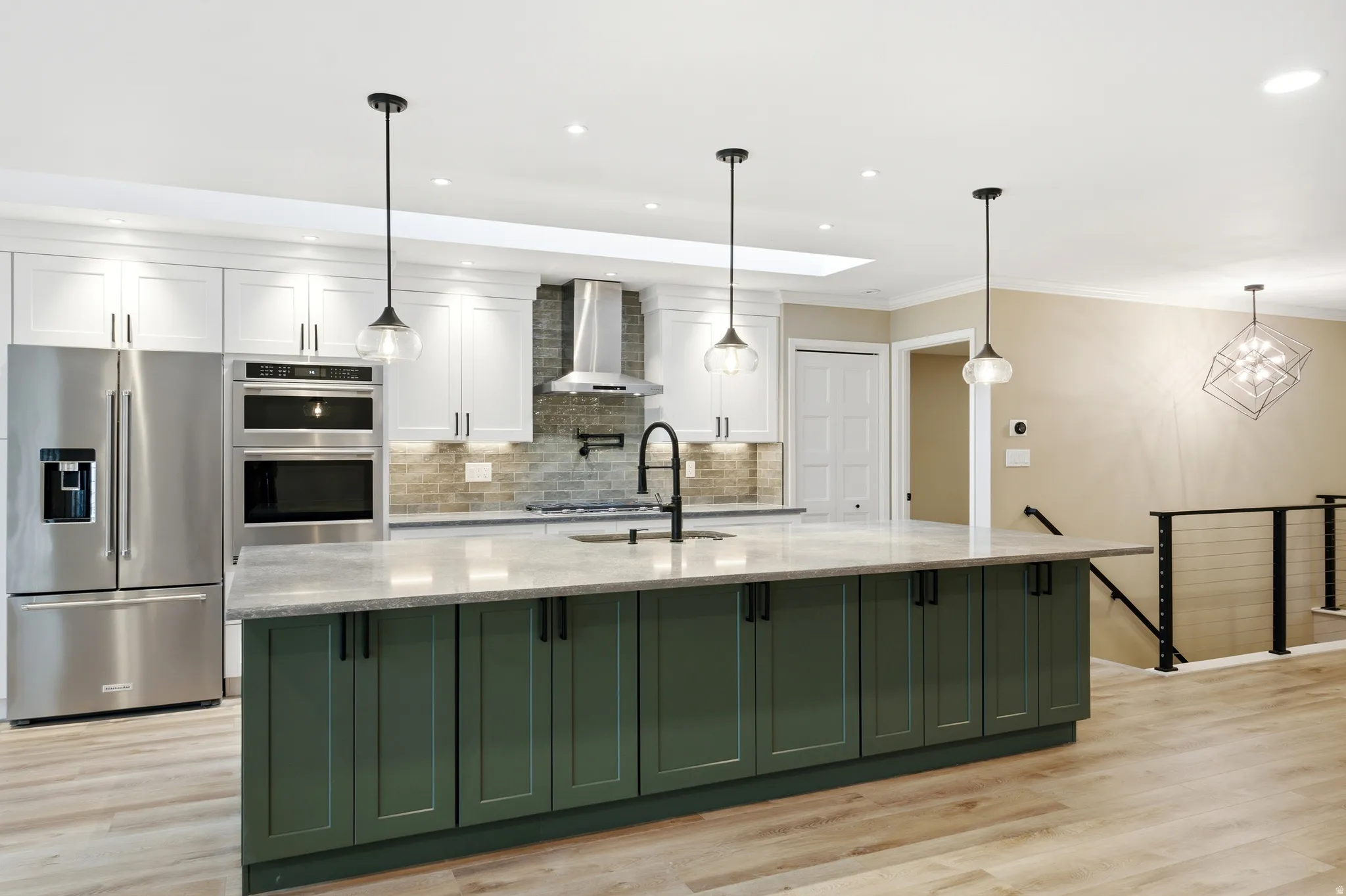 Gourmet kitchen featuring a substantial island with dark green cabinetry, stainless steel appliances, light wood-finish flooring, white upper cabinetry, and a skylight