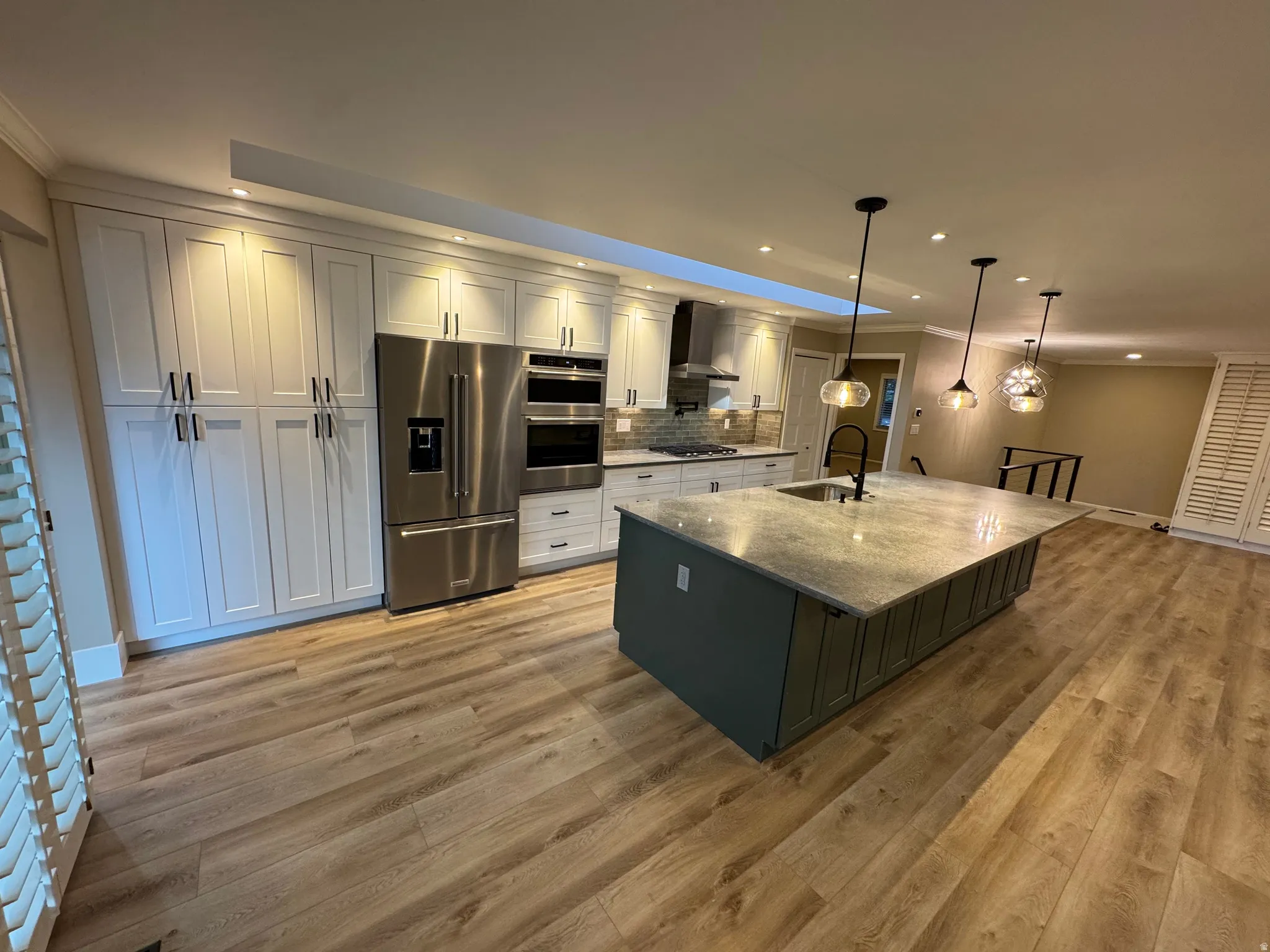 Modern kitchen featuring a large island with sink, stainless steel appliances, extensive white cabinetry, recessed lighting, and wood-finish flooring