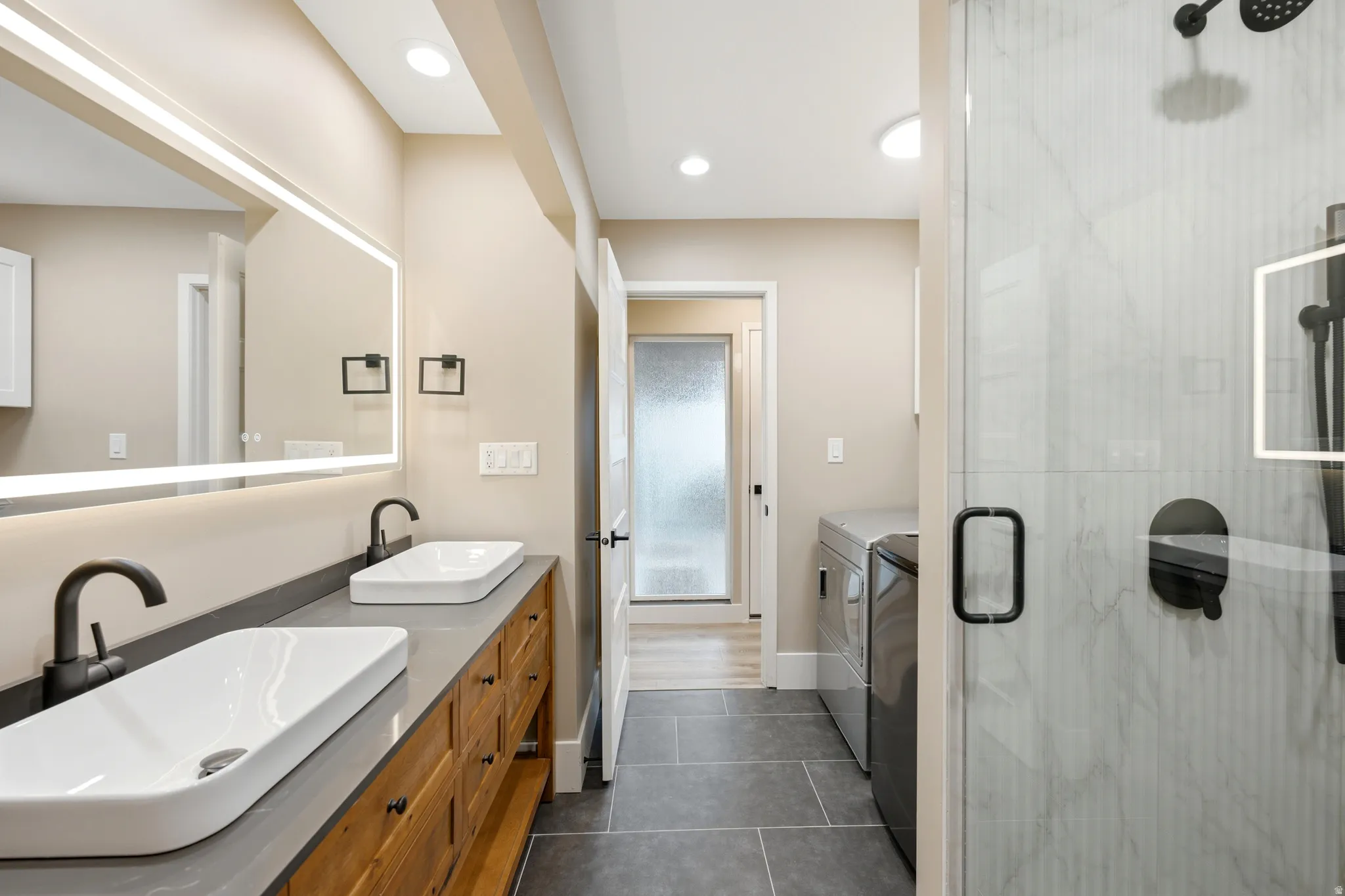 Bathroom featuring a spacious double vanity with vessel sinks, wood-finish cabinetry, and a lighted mirror
