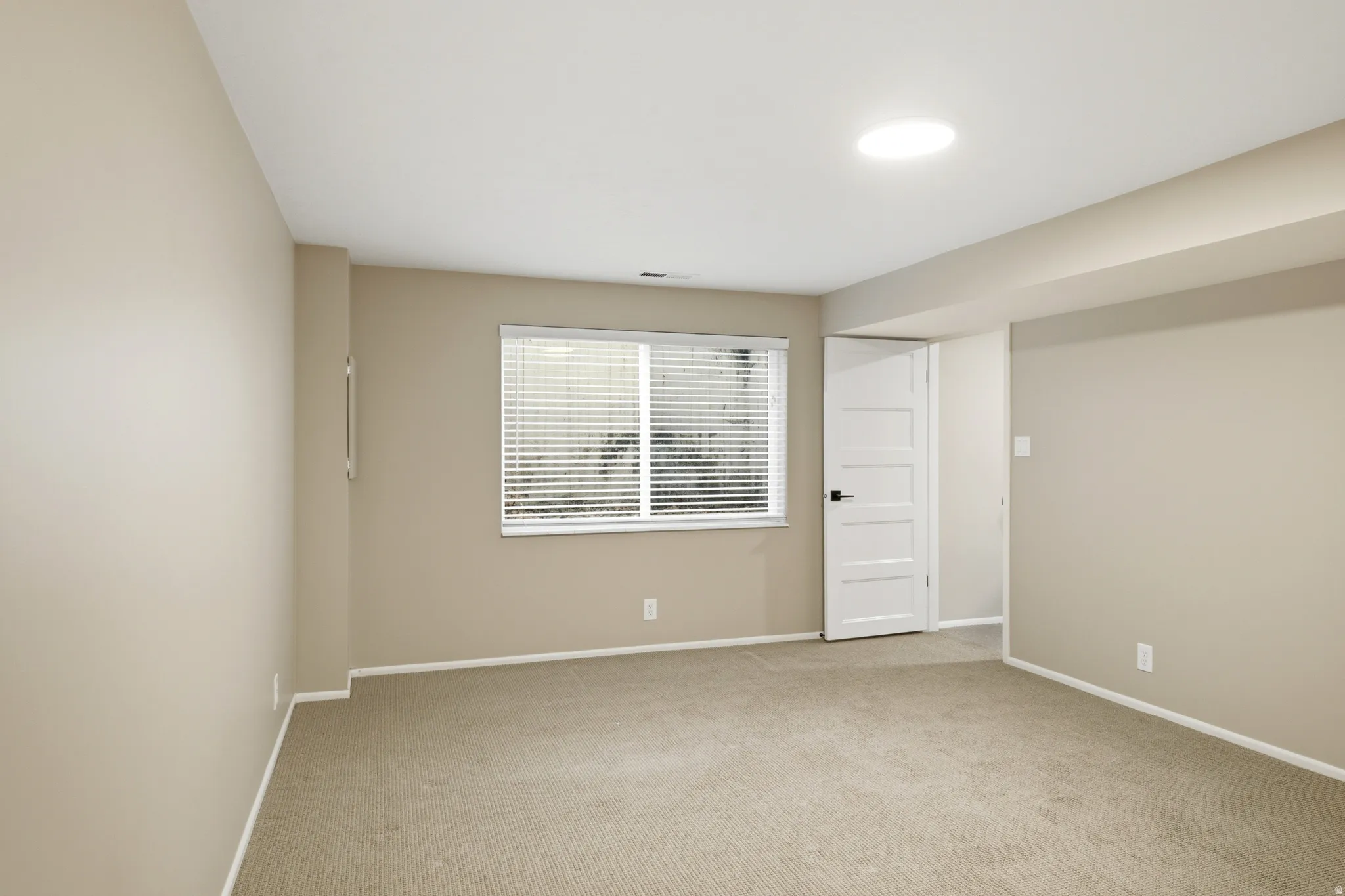 Carpeted room featuring a single window with blinds, a modern paneled door, light neutral wall tones, and recessed ceiling lighting