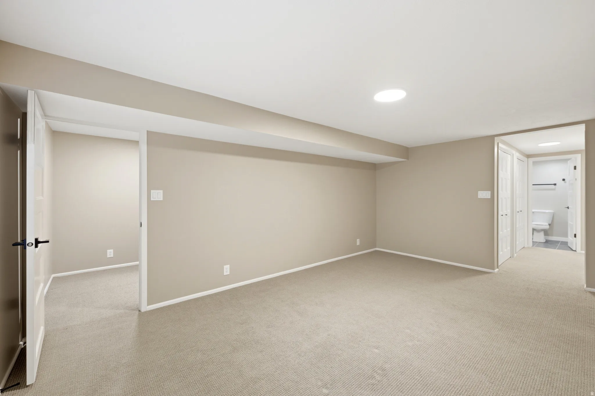 Spacious room featuring neutral carpeting, light beige wall paint, white trim, recessed lighting, and access to a separate room and bathroom