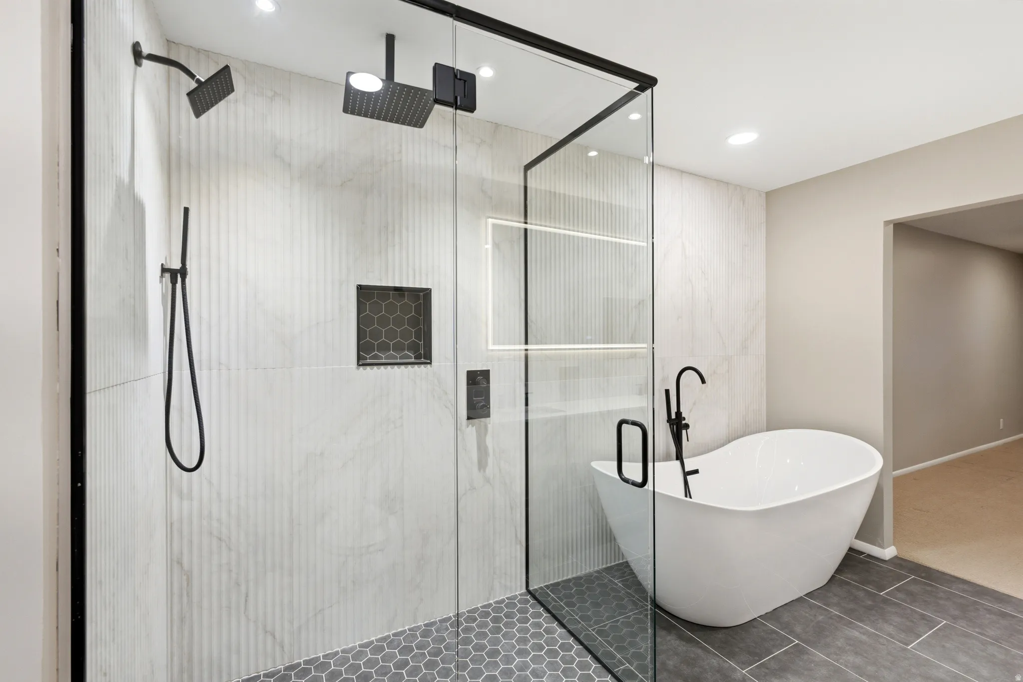 Contemporary bathroom featuring a frameless glass shower enclosure with matte black fixtures, a built-in shower niche with hexagonal tile, and a freestanding soaking tub with a floor-mounted faucet