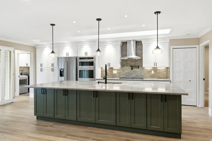 Spacious kitchen featuring a large island with dark green cabinetry and a light-toned countertop, complemented by white upper cabinetry and stainless steel appliances